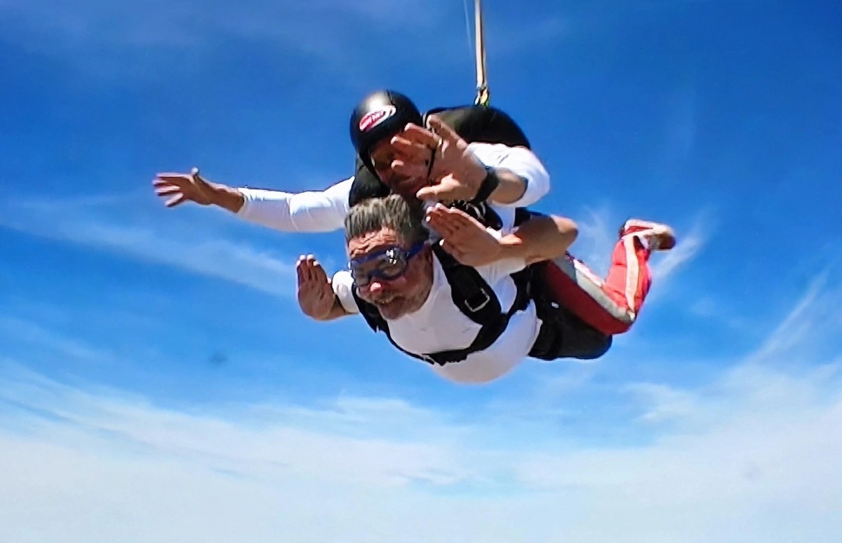 José Luis Gimeno en caída libre, saltando en paracaídas en tándem sobre un cielo azul, con gafas y los brazos abiertos