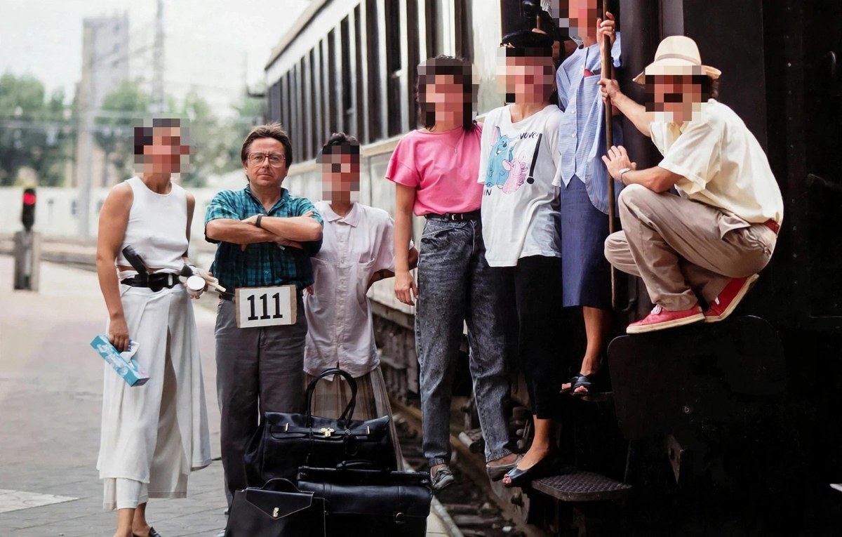 Producción para Almacenes Pyrénées en 1985: grupo de modelos y equipo junto a un tren en una estación, con un hombre de gafas con el cartel 111 sobre el cinturón