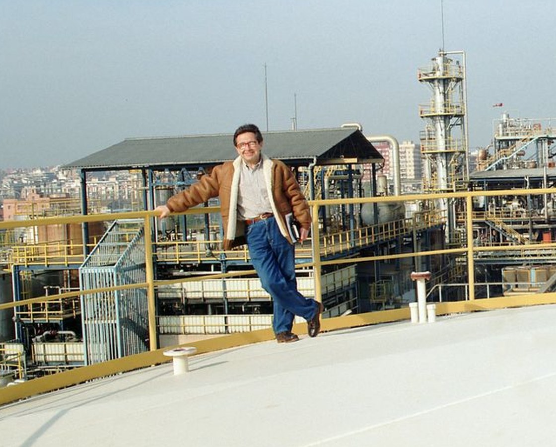 José Luis Gimeno con chaqueta de borrego apoyado en una barandilla amarilla sobre el techo de un depósito, con una planta química al fondo